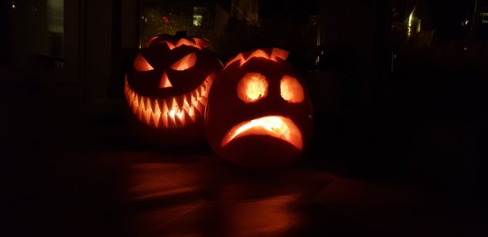 Två upplysta halloweenpumpor med utskurna ansikten i mörkt rum.