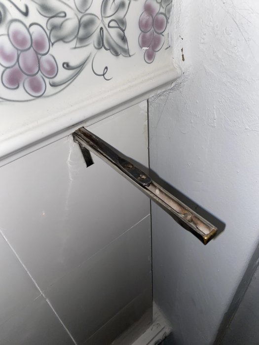 Arm av spjället på kakelugnen utan kedja mot kaklat och vitmålat vägg.