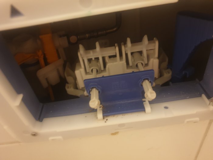 Inre mekanismen i en toalettstol med öppen service lucka, inkluderar spolknappar och kopplingar.