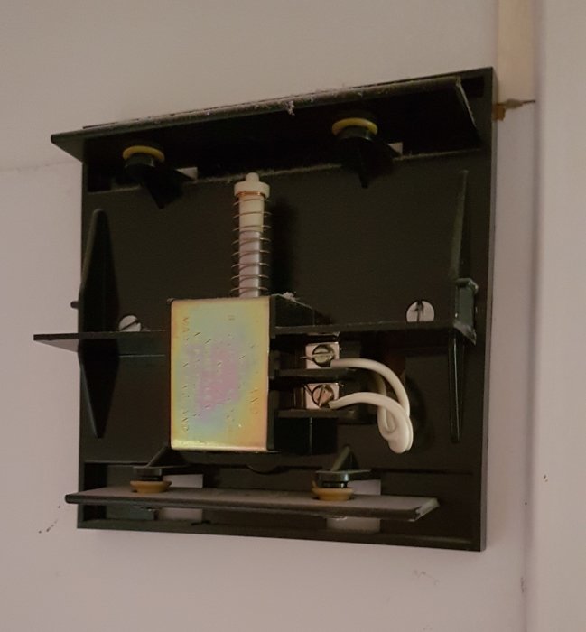 Gammal dörrklockas mekanism med fjädrar och transformator monterad på vägg.