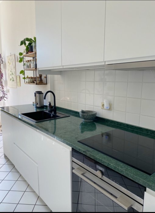 Modernt vitt kök utan knoppar med matta luckor, grepplist, grön marmorbänkskiva och inbyggda vitvaror.