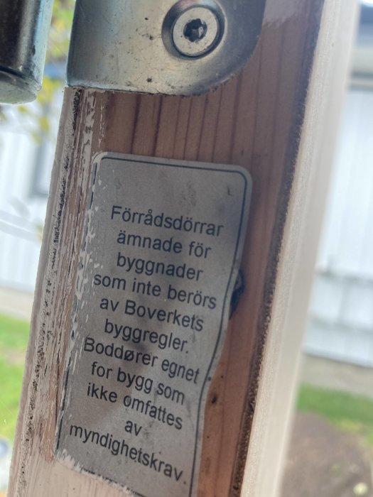 Närbild på etikett vid dörrens gångjärn med text om byggregler för förvaringsdörrar.