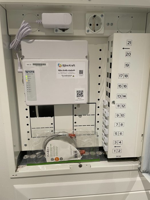 Nätverksskåp med öppen fiberbox, nätverksuttag och nätverkskablar i en bostad.