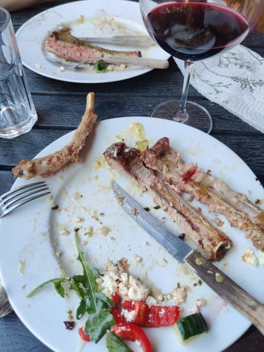 Nästan uppätna lammracks med några grönsaksbitar kvar på tallriken och ett glas rödvin.