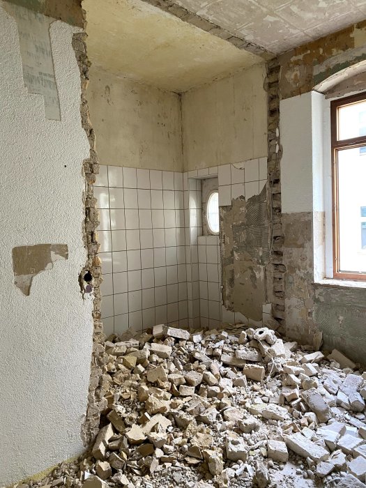 Nedriven vägg med tegelstenar och grus på golvet i ett halvrenoverat rum.