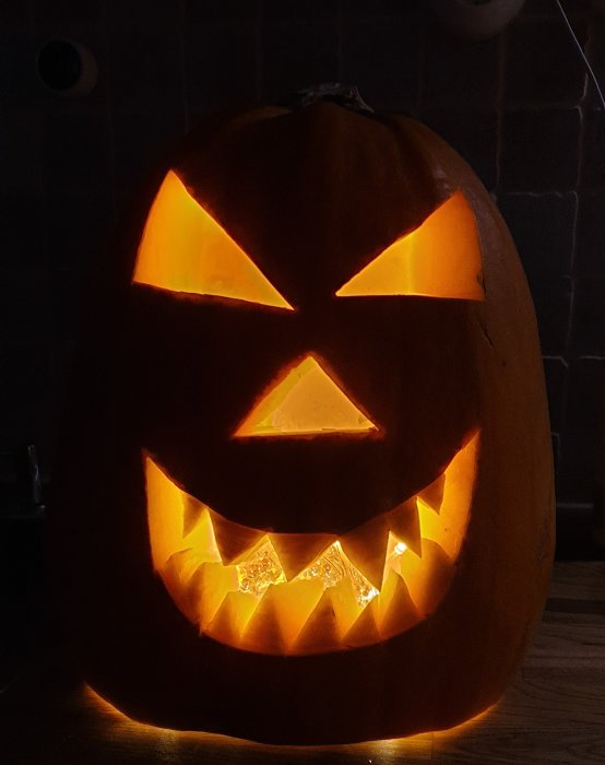 Upplyst utskuren halloweenpumpa med sned ögon och skrämmande leende.