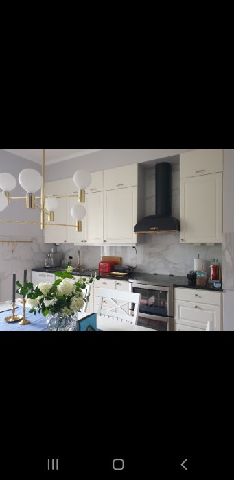 Klassiskt kök med vitlackade luckor, marmorbakgrund och moderna gulddetaljer samt vitvaror.