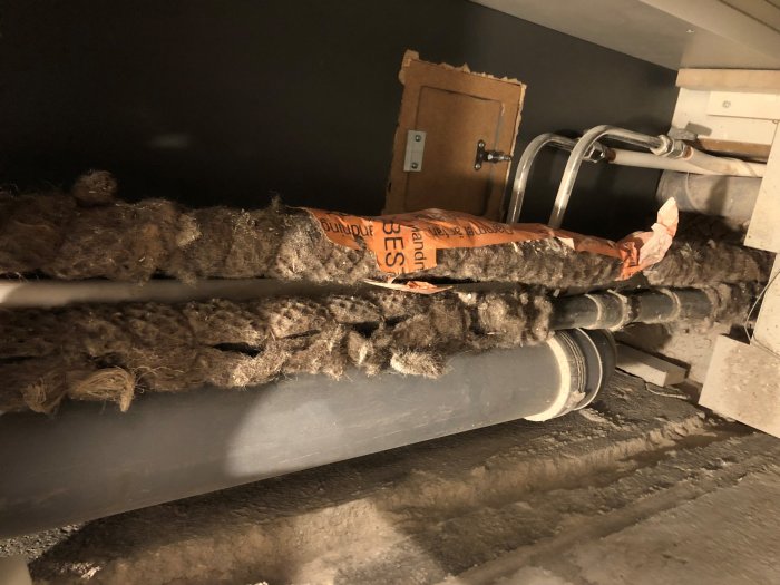 Rör med ullliknande isolering och varningslapp om asbest under renovering.