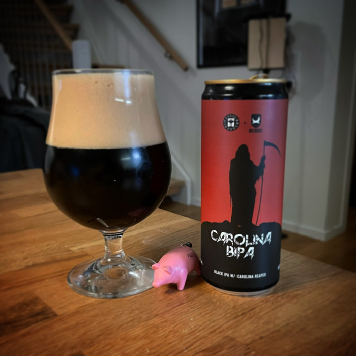 En mörk chiliöl i glas bredvid burken och en liten rosa plastgris på ett träbord.