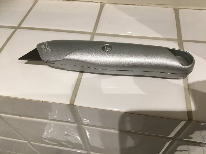 En hopfällbar kniv med ett kort blad på ett kaklat underlag.