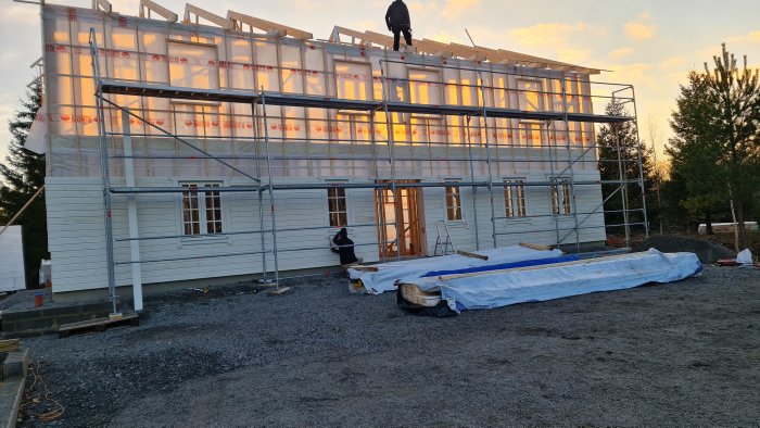 Två personer monterar fönster på ett nybyggt hus med synligt träarbete och skyddsplast.