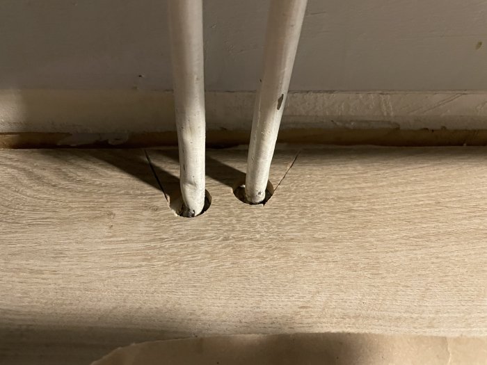 Närbild på ett golv med två vita rör som går igenom utan rörmanchetter.
