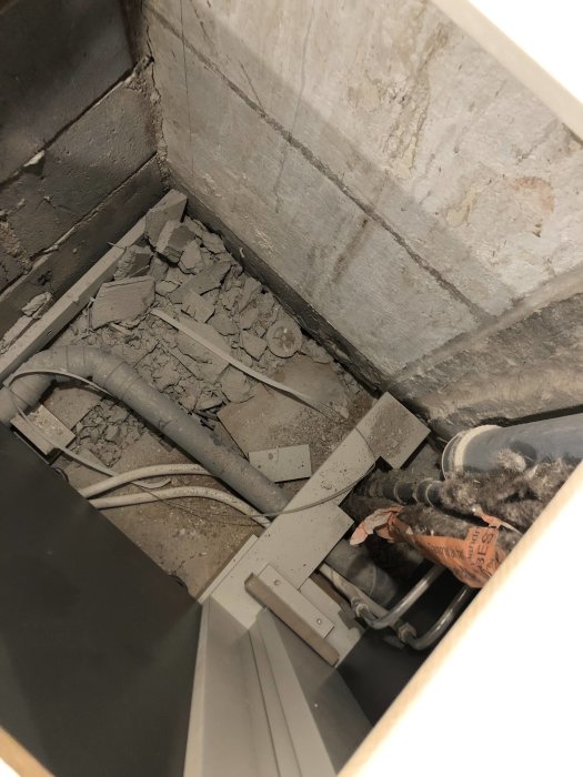 Rörsystem och mycket byggdamm i hörnet av ett kök, ej städat, redo för bänkskivan.