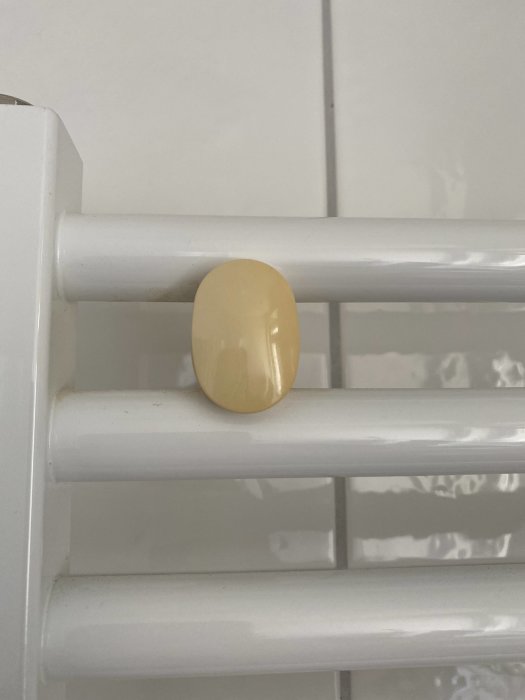 Vit väggmonterad vattenradiator med en beige fästplatta mot kakelvägg.