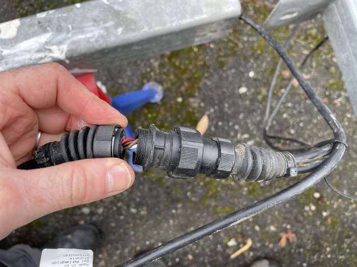Hand håller en delad elkabelanslutning med synliga ledningar, avsedd för skarvning på en släpvagn.