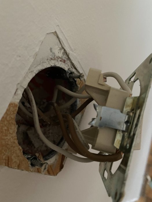 Öppet eluttag i vägg med anslutna bruna och vita kablar och en gammal strömbrytare.