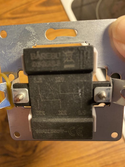 Närbild av en elbrytare hållen i en hand med märkningen "BAREBO" och ledningsterminaler synliga för installation.