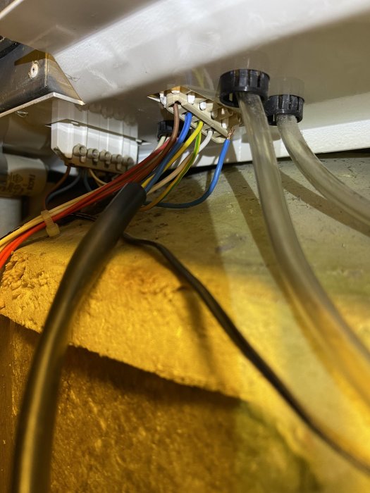 Elkablar och kontaktblock under värmepanna, lösa blå och gula sladdar synliga.