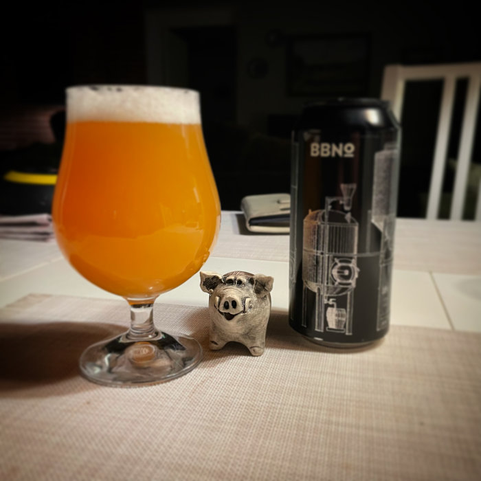 Ett glas med orangefärgad dryck, en ölburk och en liten grissparbössa på ett bord.