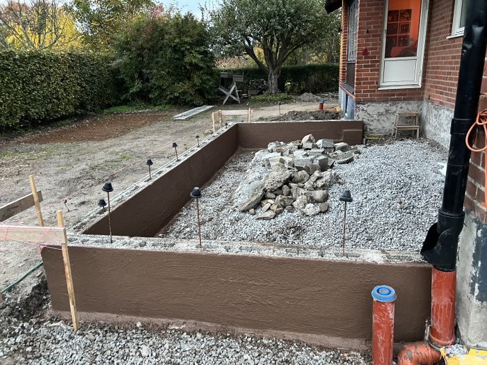 Grundarbete med platonmatta och grus inför isolering och gjutning för renovering nära hus.