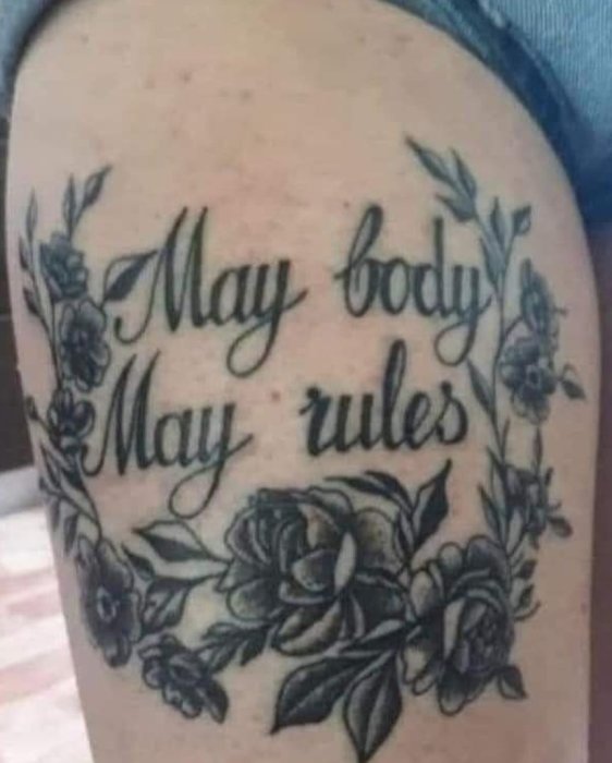 Tatuering på arm med texten "May body May rules" omgivet av blommönster.