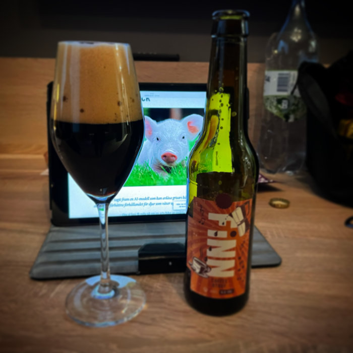 Ett glas mörkt öl och en ölflaska framför en surfplatta som visar en bild av ett grisungar.