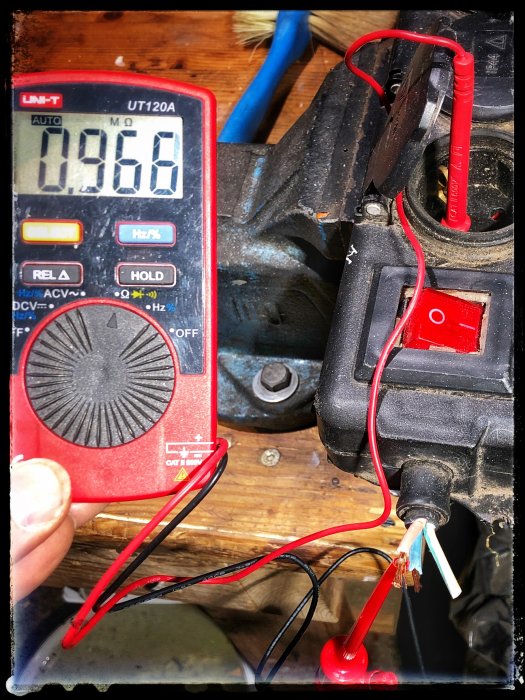 Multimeter som visar 0.966 MΩ testar motståndet på en klippt sladd kopplad till grenuttag.