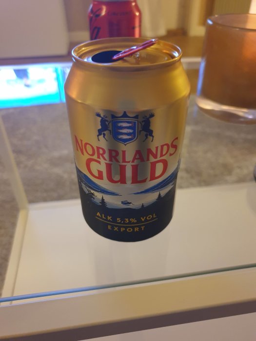 En öppnad ölburk av märket Norrlands Guld på ett glasbord.