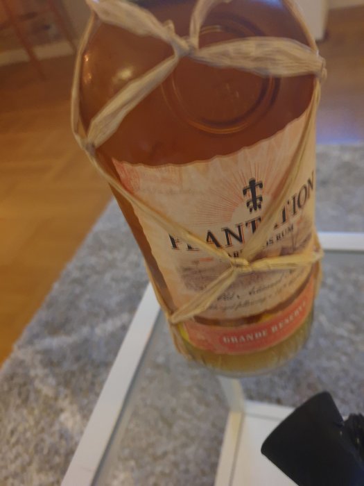 Flaska med rom omsluten av ett snöre, placerad på bord med oskarp bakgrund.