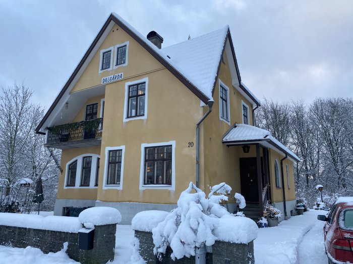 Välbevarat gult hus med snötäckt tak och omgivning under vinter.