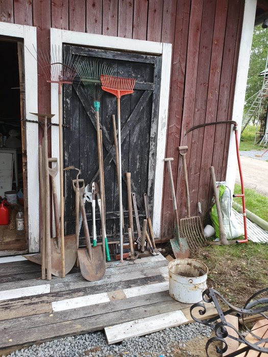 Sortiment av trädgårdsredskap lutade mot en röd träbyggnad vid ombyggd träbro.