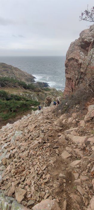 Vandrare på en stig med lösa stenar längs en klippig kust.