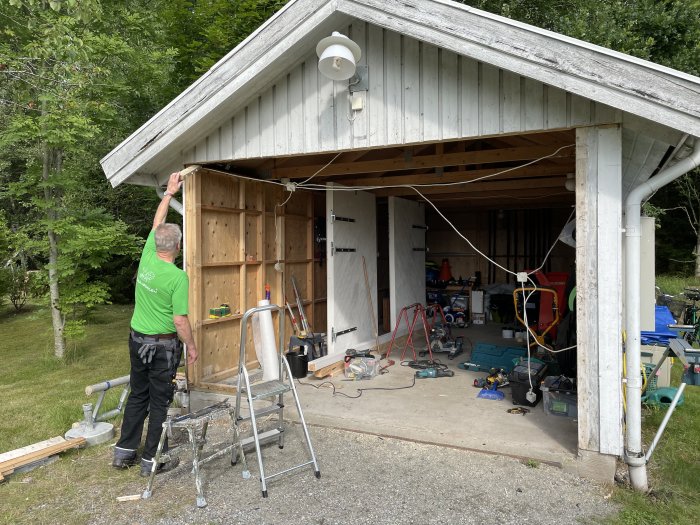 Person monterar plywoodskivor på kallgaraget med öppen port och verktyg utspridda.