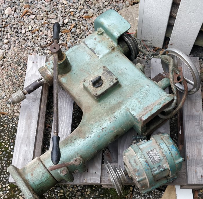 Gammal sliten grön stationsär motorpump på grusunderlag.