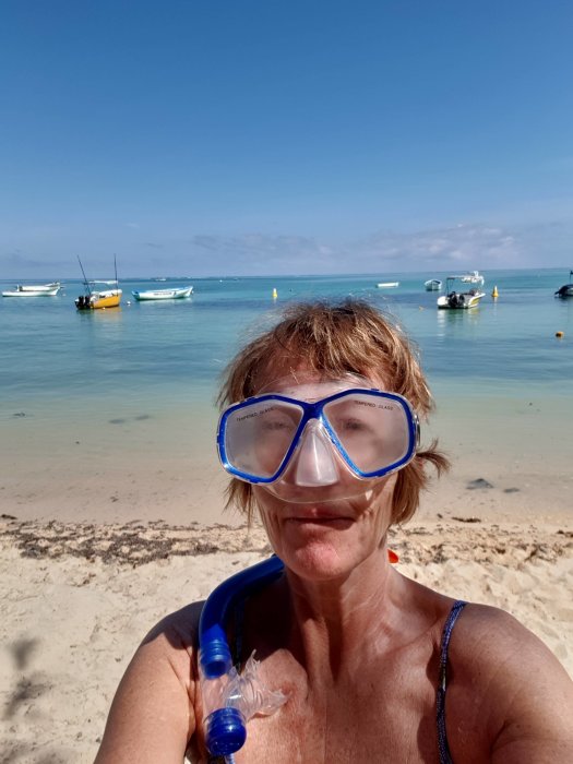 Person med dykmask och snorkel framför en strand med båtar i vattnet.