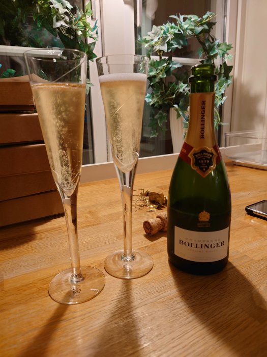 Två champagneflöjter med bubblig dryck och en flaska Bollinger champagne på ett bord.