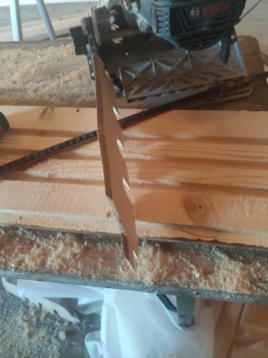 Cirkelsåg som skär genom en tjock träpanel på ett arbetsbord med sågspån omkring.