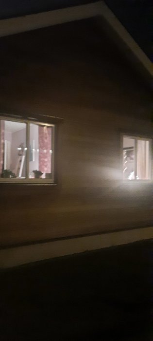 Yttervägg av hus på kvällen med två synliga fönster och område mellan där en lampa önskas monteras utan synlig kabel.