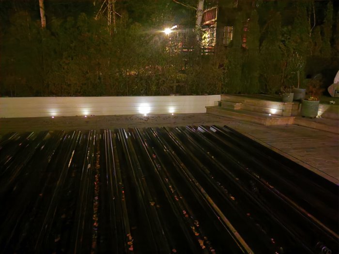 En altan på kvällen med svagt lysande och några helt släckta 12v utomhuslampor längs kanten, omgiven av mörk natur.