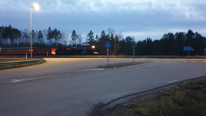 Tom rondell vid skymning med vägskyltar som pekar mot Falun och Rättvik, och ett suddigt tåg i bakgrunden.