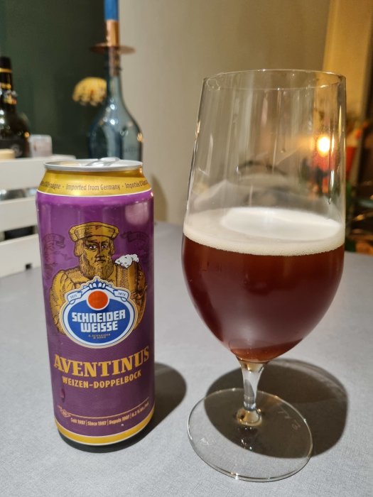 En Aventinus Weizen-Doppelbock ölburk bredvid ett glas fyllt med mörk öl, på en bordsskiva.