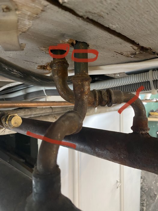 Gamla rör under golv med röda streck markerade för kapning och ritade cirklar som illustrerar rörens diameter.