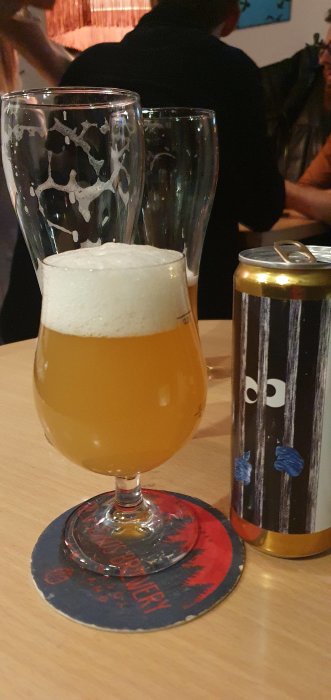 Ett glas med veteöl och skumkrona bredvid en tom burk med öl på en pub.