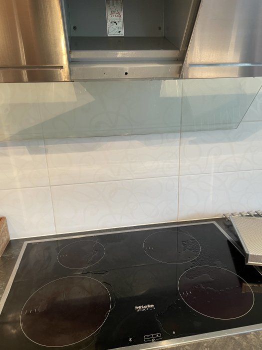 Vatten på en induktionsspis under en fläktkanal, antyder läckage vid kraftigt regn.