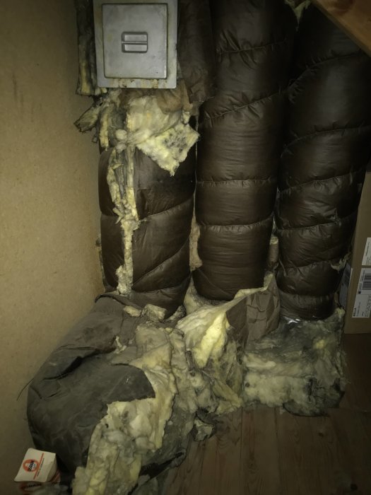 Åtkomstområdet på en kattvind med synlig isolering och rör insvepta i mörkt material.