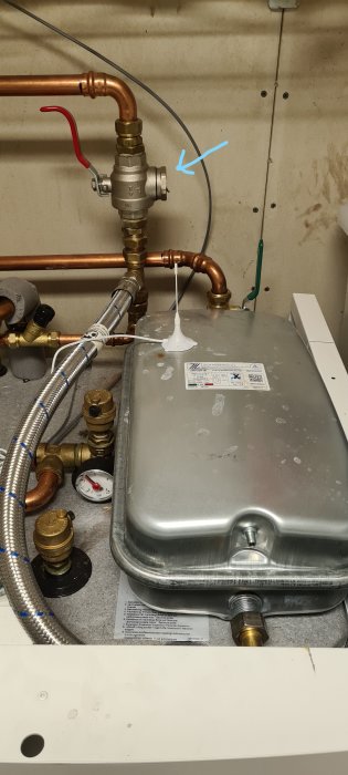 Värmepump med kopparledningar och komponenter, blå pil pekar på rensat smutsfilter på returledningen.