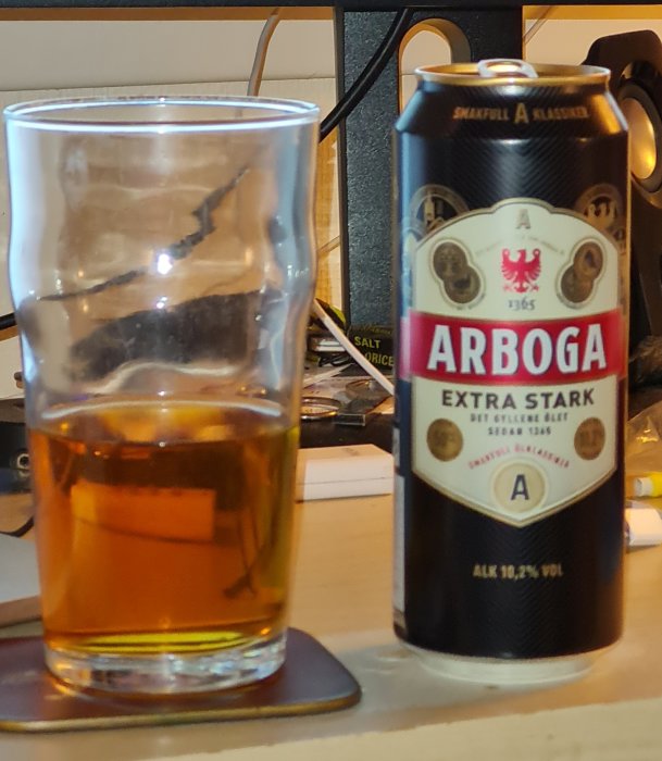 Halvfylld ölglas bredvid en burk Arboga Extra Stark öl på ett skrivbord.