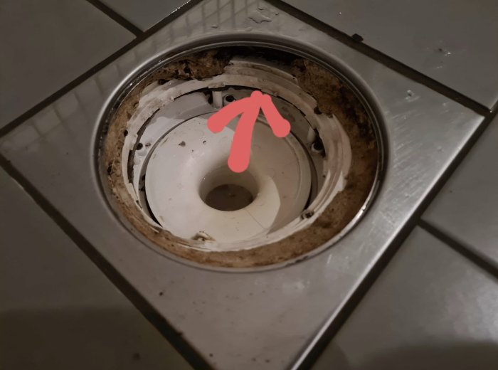 Närbild av en duschsluk med synligt hål och saknad cement runt kanten, indikerande potentiellt underhållsproblem.