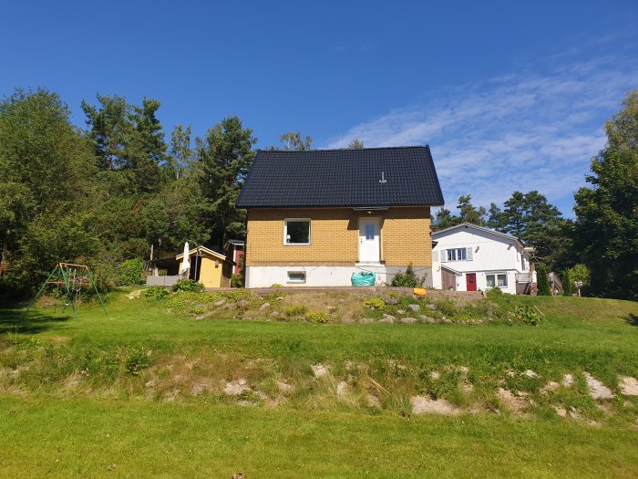 Hus och trädgård före renovering med synligt markarbete och en gammal gungställning.