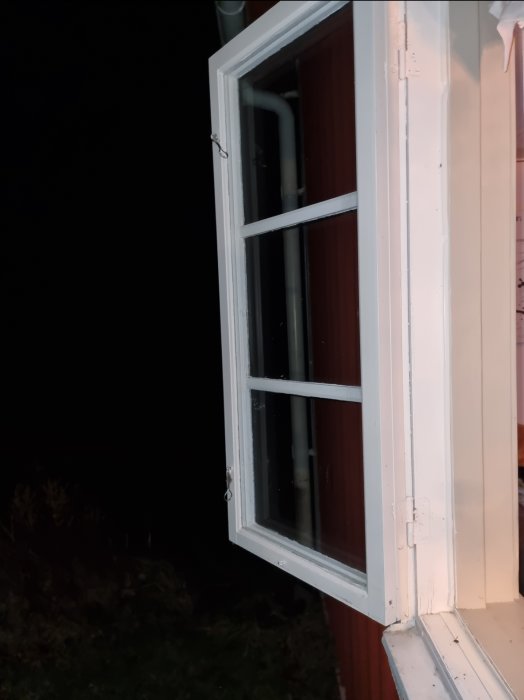 Vitfönstrad fönsterkarm och foder på en röd husvägg i dunkel belysning, osäkerhet kring innerstrukturen uttrycks.
